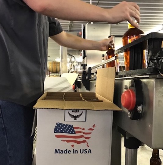 A man putting two whiskey bottles into a cardboard box that has an American flag on it