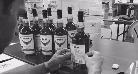 One of the owners of Valor Spirits hand placing a label onto a whiskey bottle